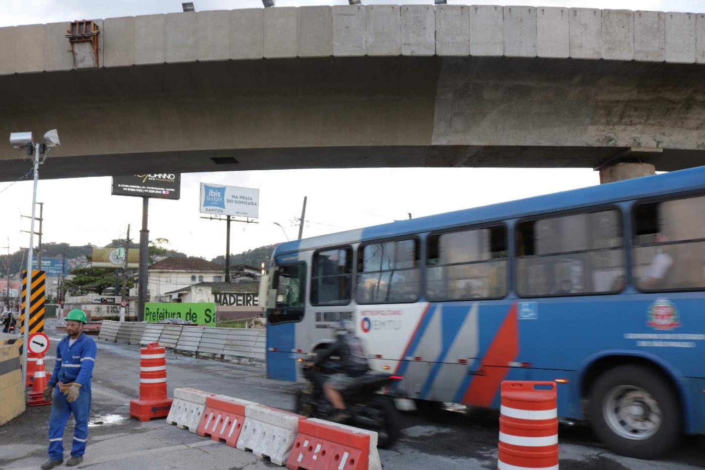 Ônibus municipal passa em via sob viaduto. #Paratodosverem