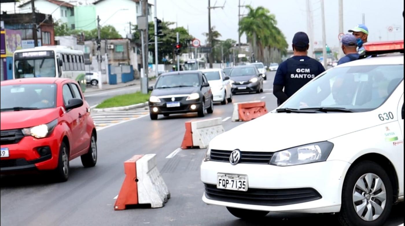 Viatura parada na via ao lado de cones que demarcam a pista. Guarda municipal e outros aguentes olham para o movimento de veículos. #Paratodosverem