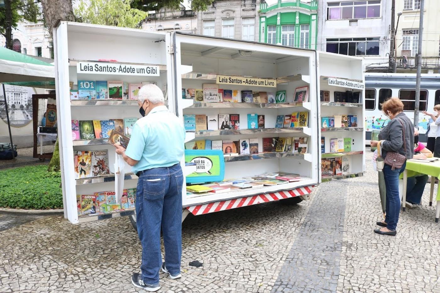 Duas pessoas olham livros e gibis em estande do Leia Santos #paratodosverem