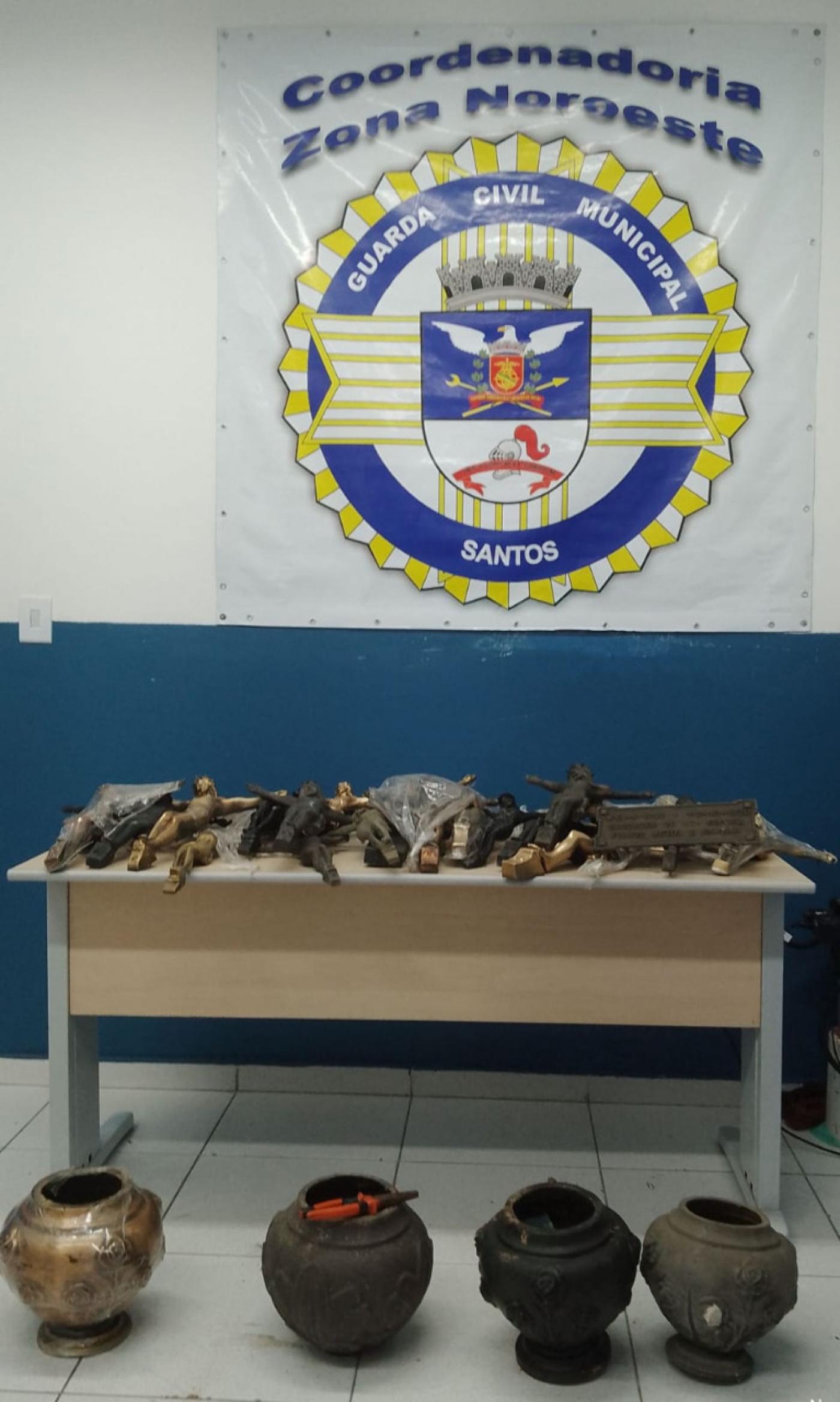 mesa com diversas peças em bronze. Ao fundo, um banner da Coordenadoria da Guarda Municipal da Zona Noroeste 