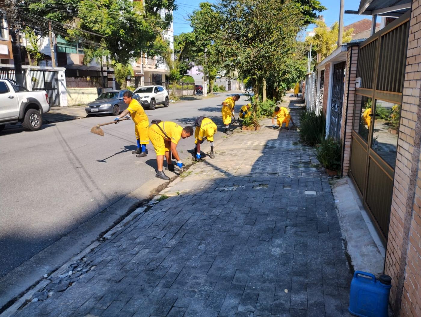 equipe de homens uniformizados capina meio-fio em rua. #paratodosverem 