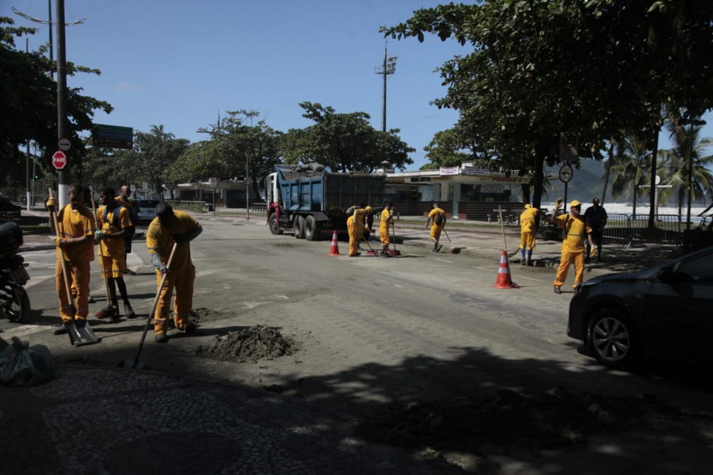 Homens removem areia de pista afetada por alagamento na Ponta da Praia. #Paratodosverem