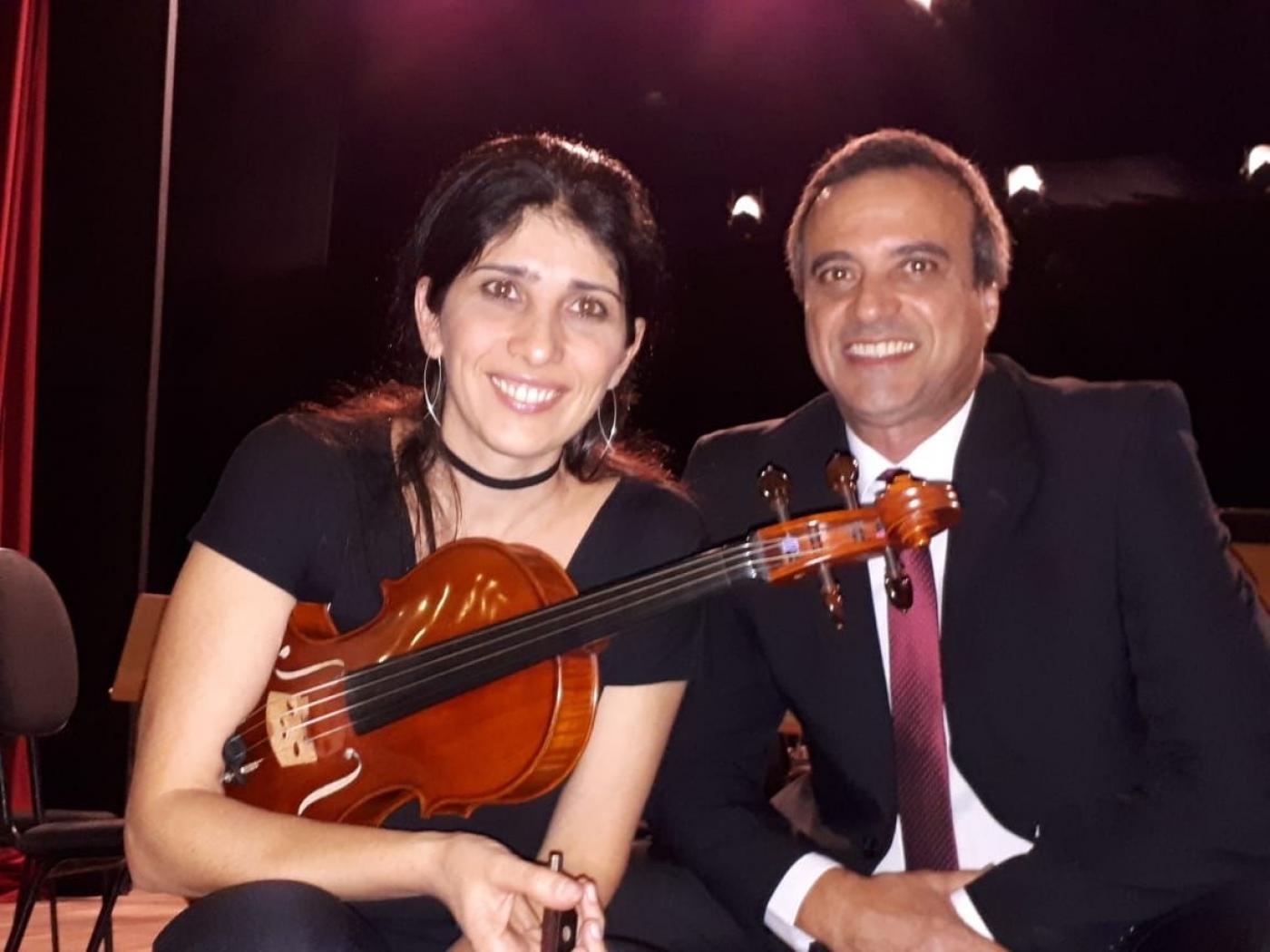 mulher e homem sentados e ela segura violino #paratodosverem