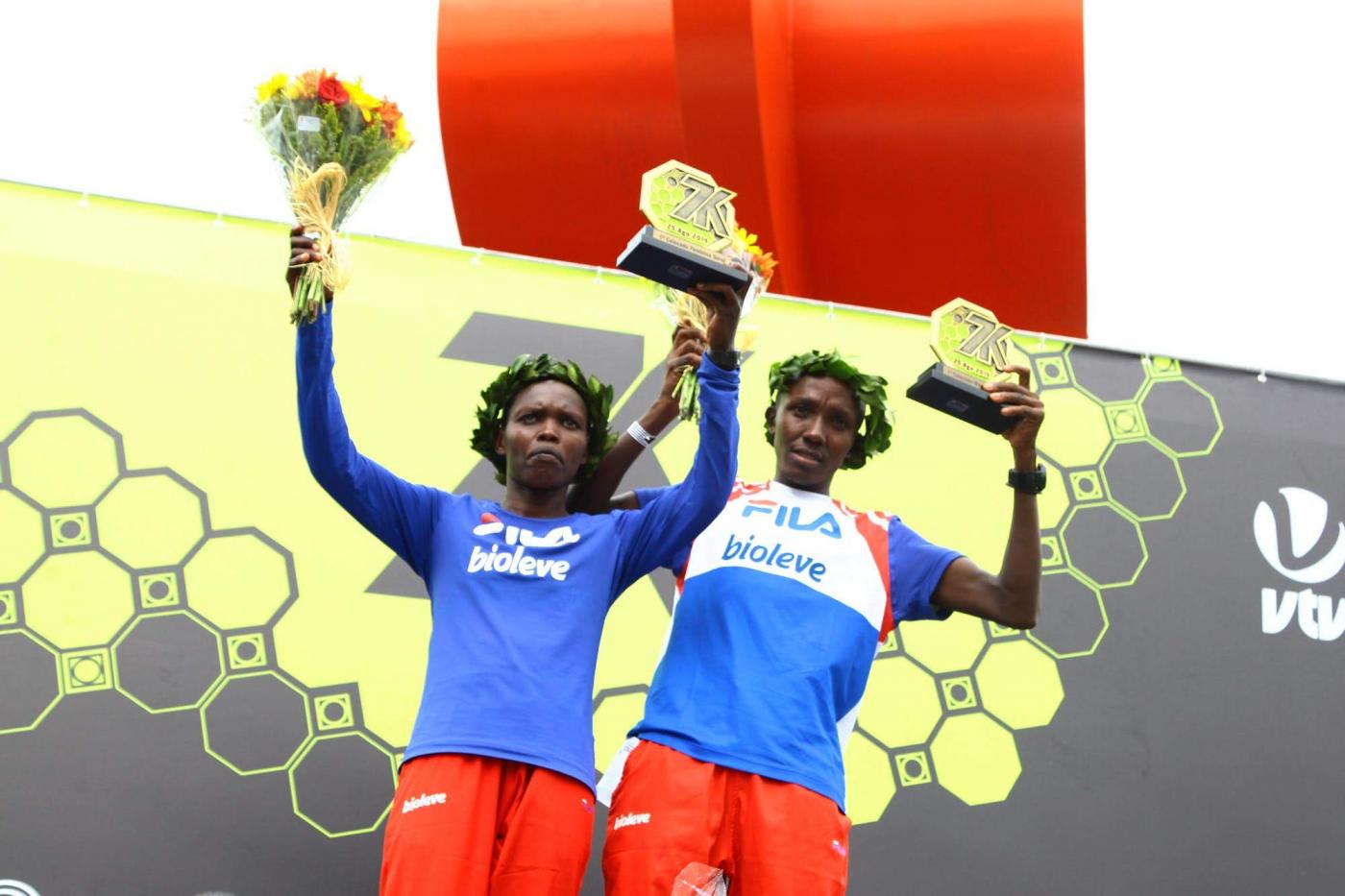 Viola Muneira Chemos e Marco Joseph erguem seus troféus. A mulher também segura um ramalhete de flores. #Pracegover