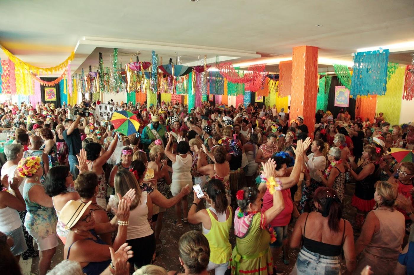baile de carnaval com salão decorado e bárias pessoas dançando. #paratodosverem