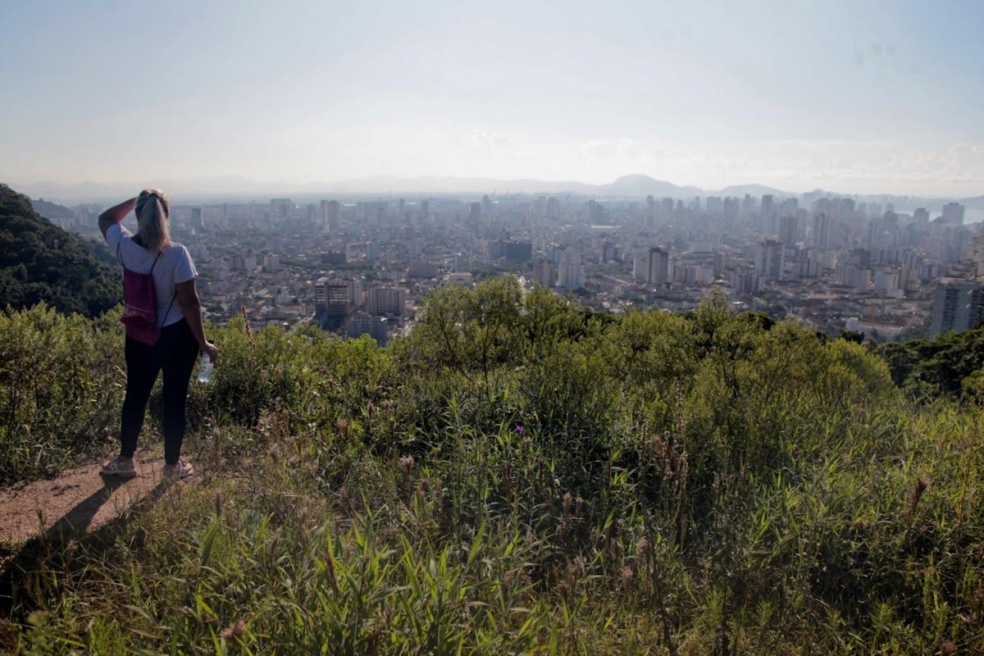 mulher está em alto de morro olhando para o horizonte. ao fundo se vê a cidade. #paratodosverem 