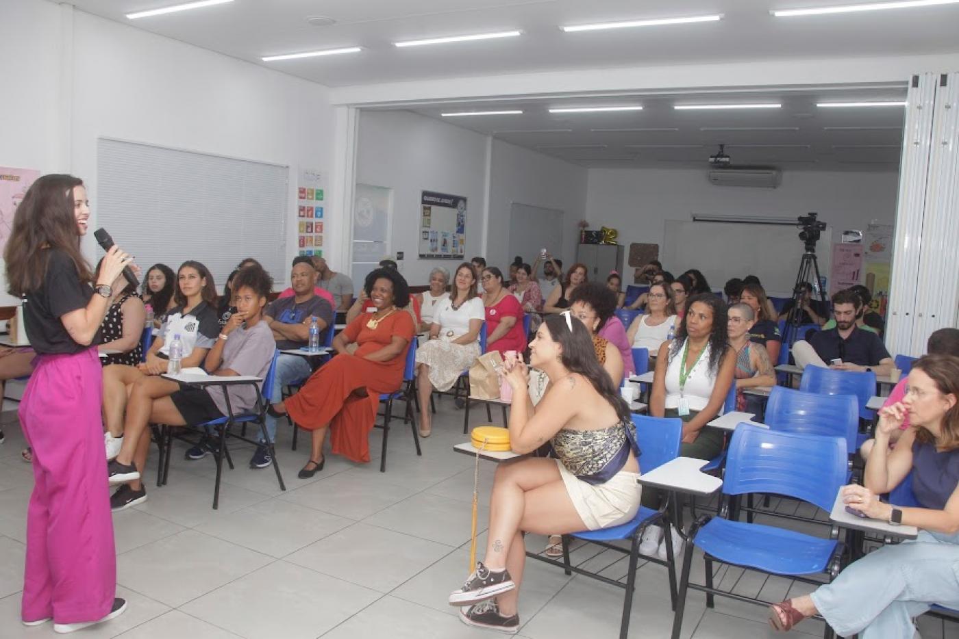 mulher dá palestra para outra mulheres que estão sentadas em uma sala. #paratodosverem 