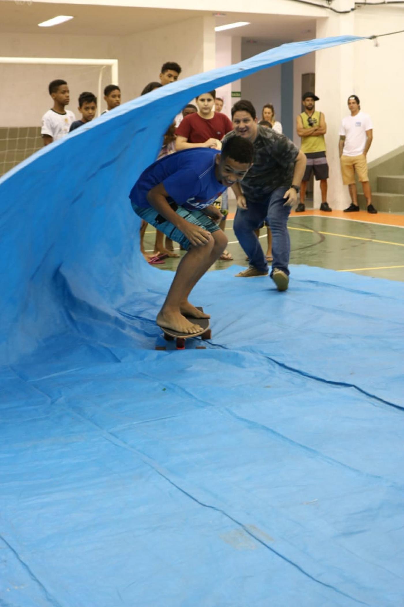 menino simula surfar em lona imitando onda #pracegover