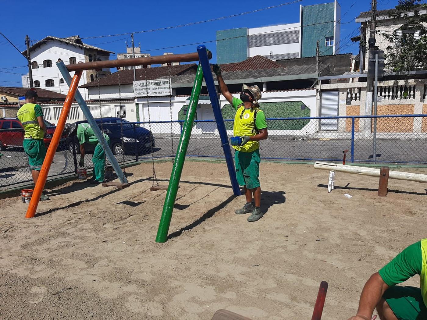 Operários pintam estrutura de balancê em playground. #paratodosverem