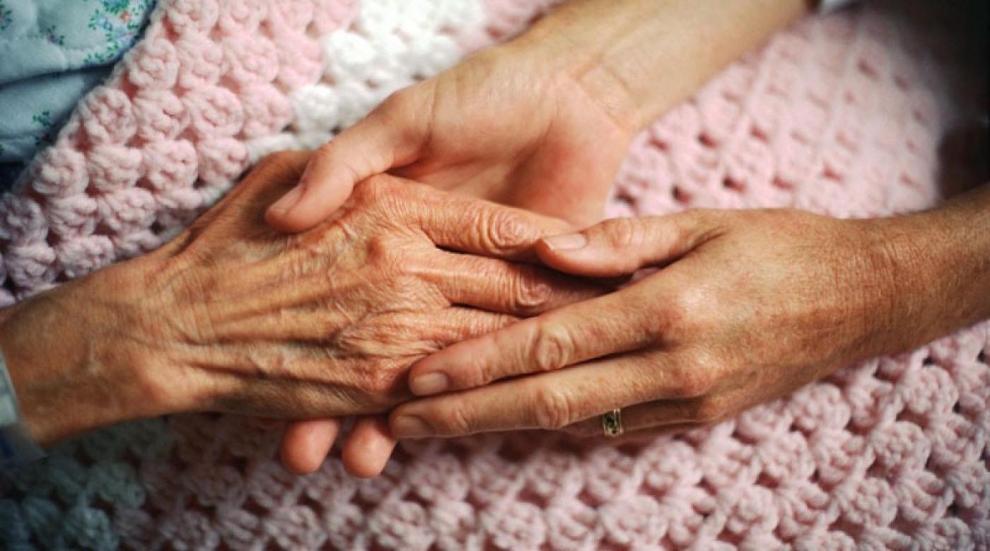 imagem em close. Mãos jovens segurando mão de pessoa idosa sobre cobertor. #paratodosverem