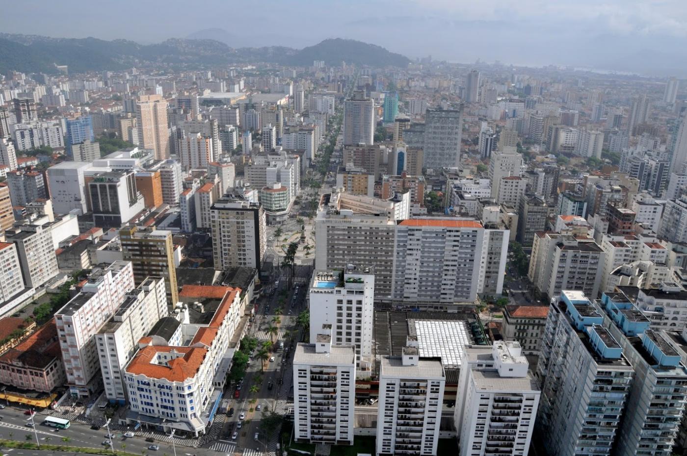 vista aérea de parte da Cidade com vário prédio e morros ao fundo. #Paratodosverem