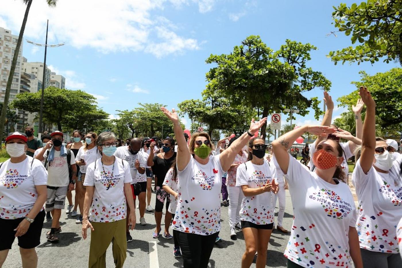 Grupo caminha pela avenida da orla debaixo de sol e vestido com camisas alusivas à prevenção do HIV. #pracegover