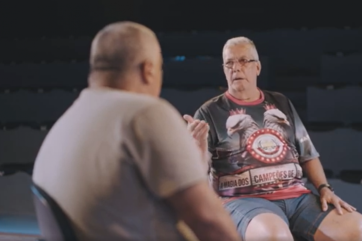 dois homens conversando, um deles de costas para a foto. #paratodosverem