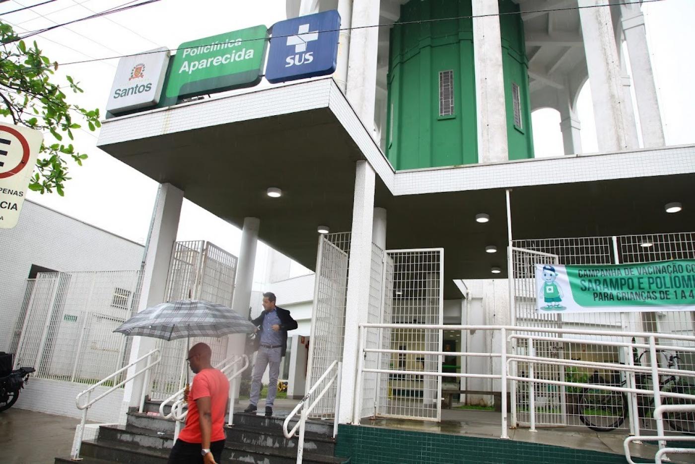 Fachada da Policlínica da Aparecida com dois homens em frente à unidade. #pratodosverem