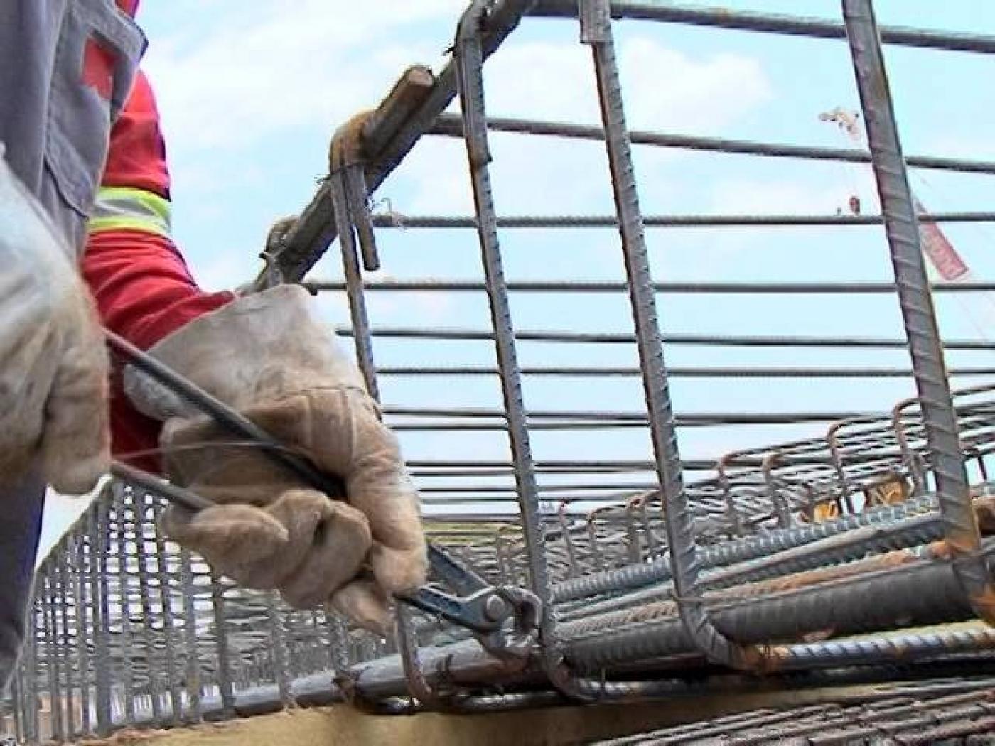 mãos com luvas e segurando alicate tocam em armação de ferro. #paratodosverem