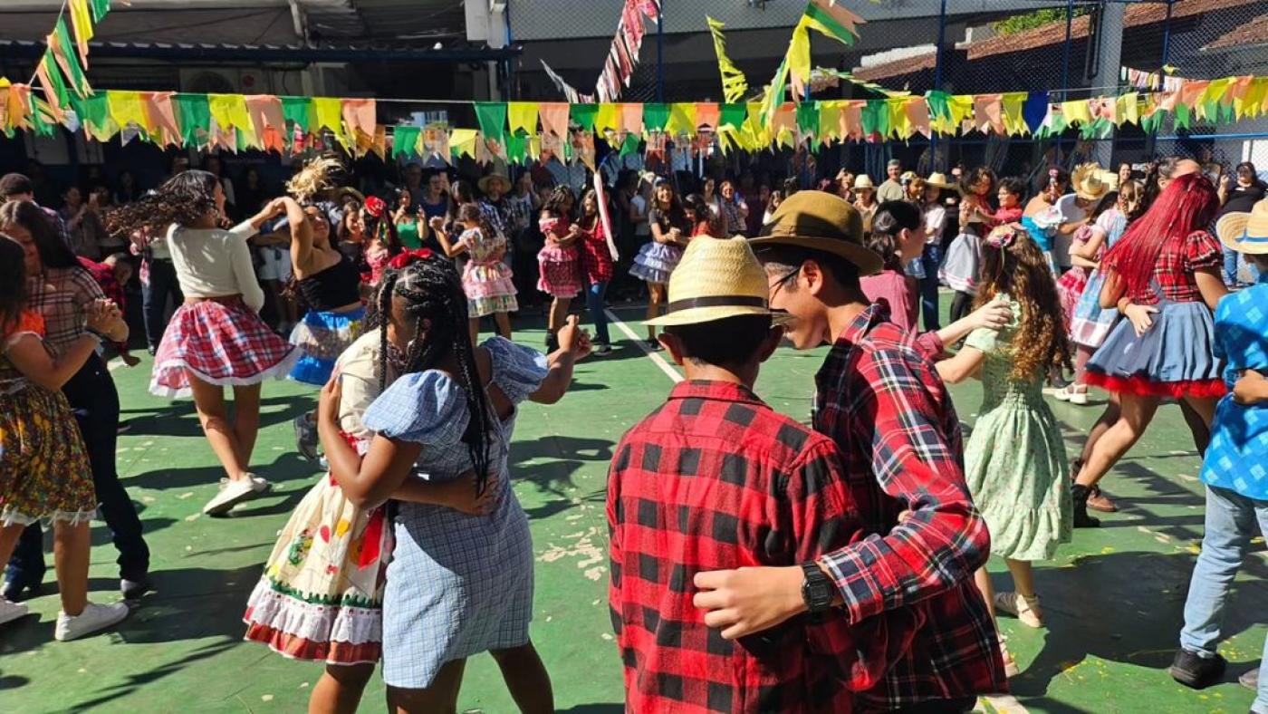crianças com roupas típicas juninas dançam em pares numa quadra. #paratodosverem 