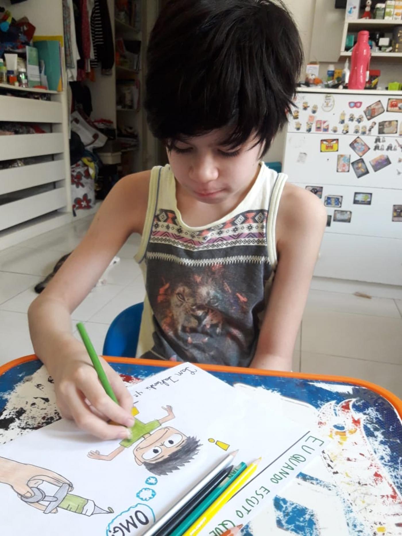 Criança está desenhando sobre uma mesa em casa. #Paratodosverem