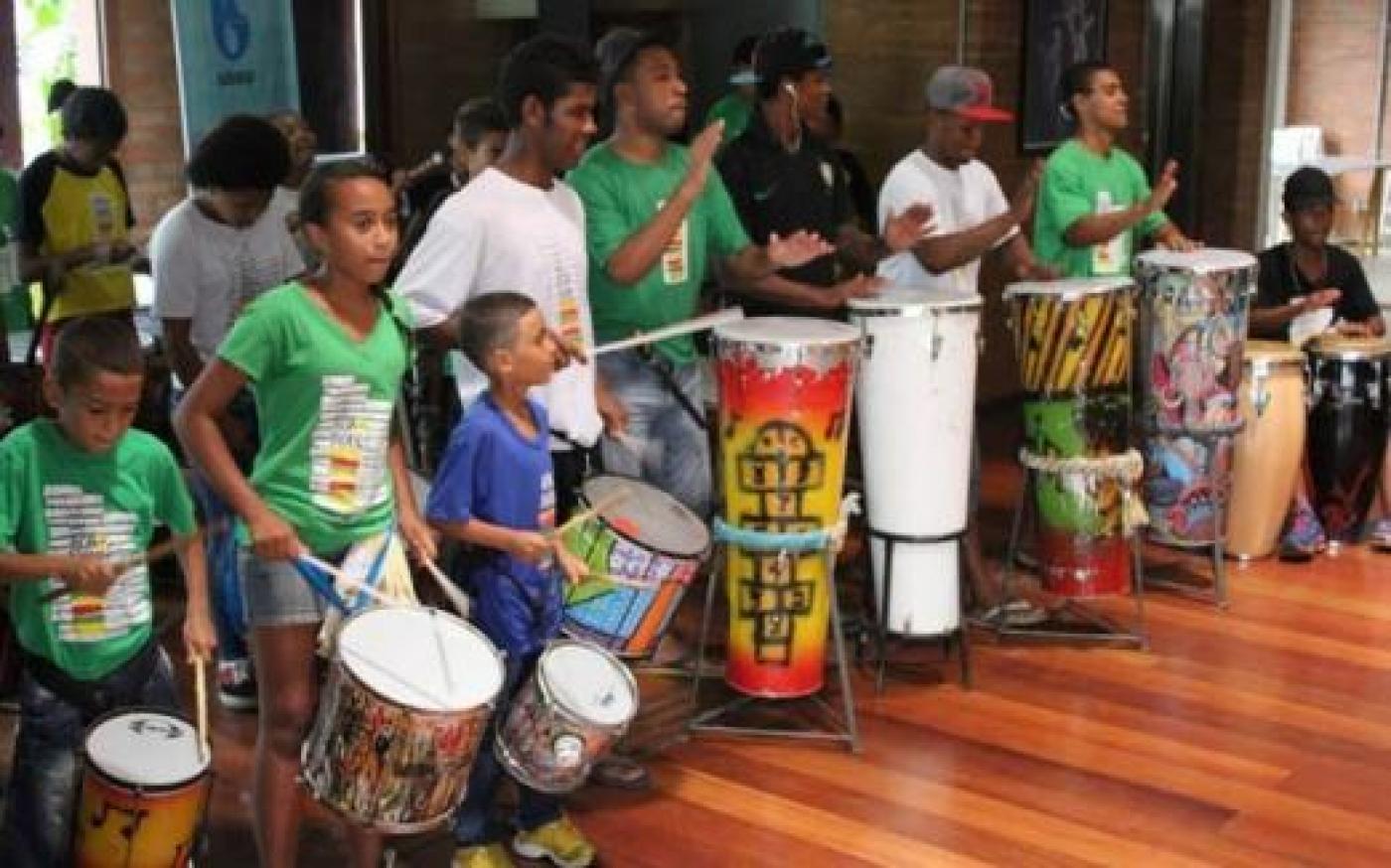 Crianças e jovens tocam instrumentos de percussão. #Paratodosverem
