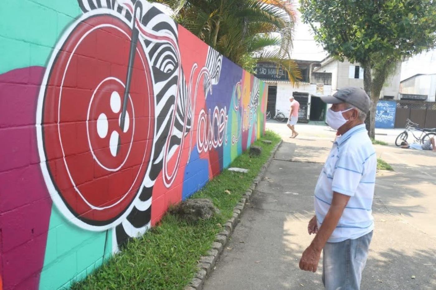grafite pintado em grande extensão de muro com homem olhando a pintura. #paratodosverem