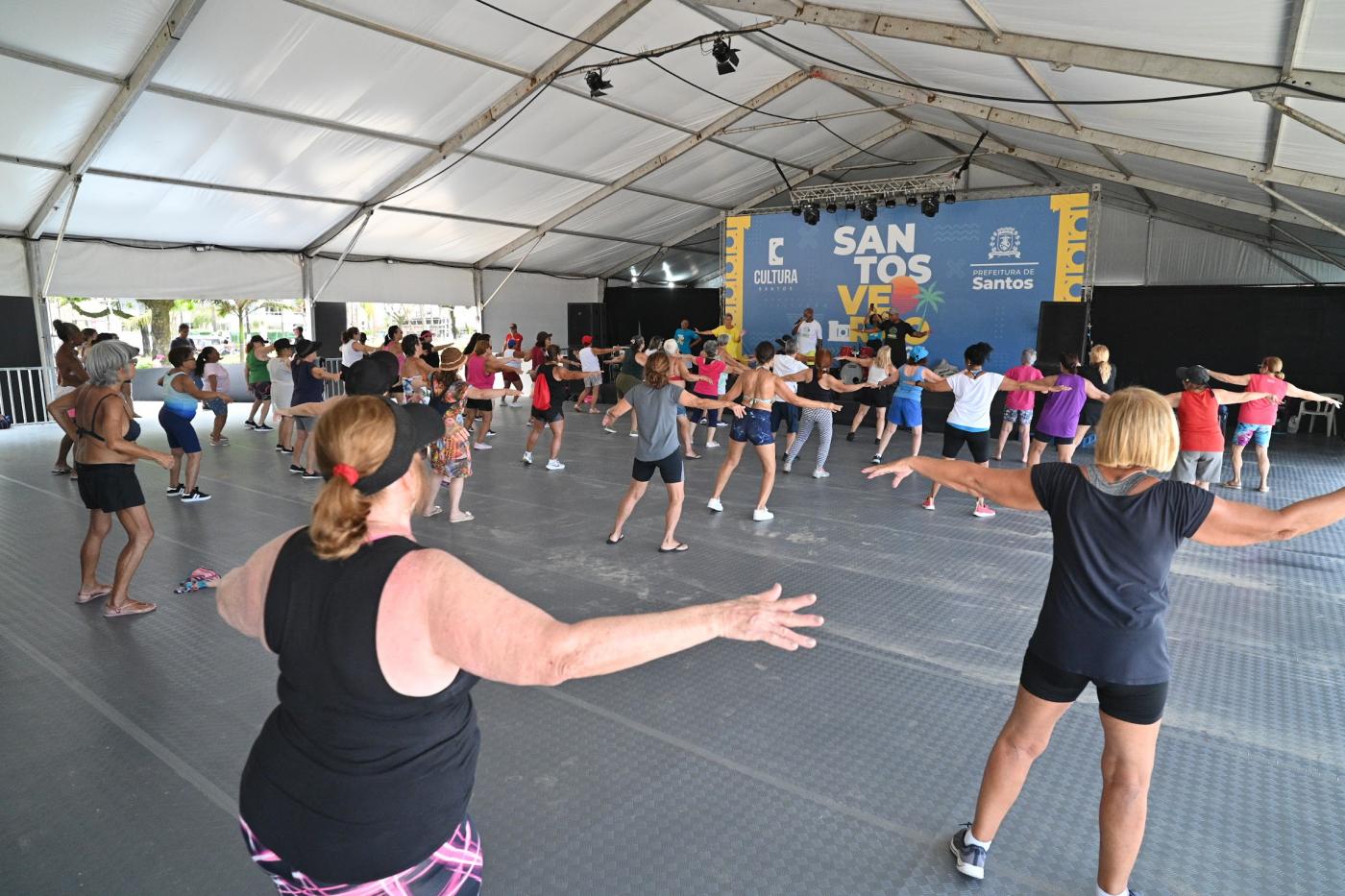 mulheres fazem alongamento sob tenda. #paratodosverem