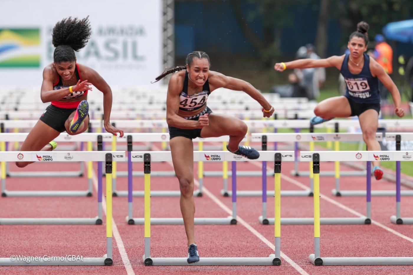 Três mulheres disputando corrida com salto em barreira. #paratodosverem