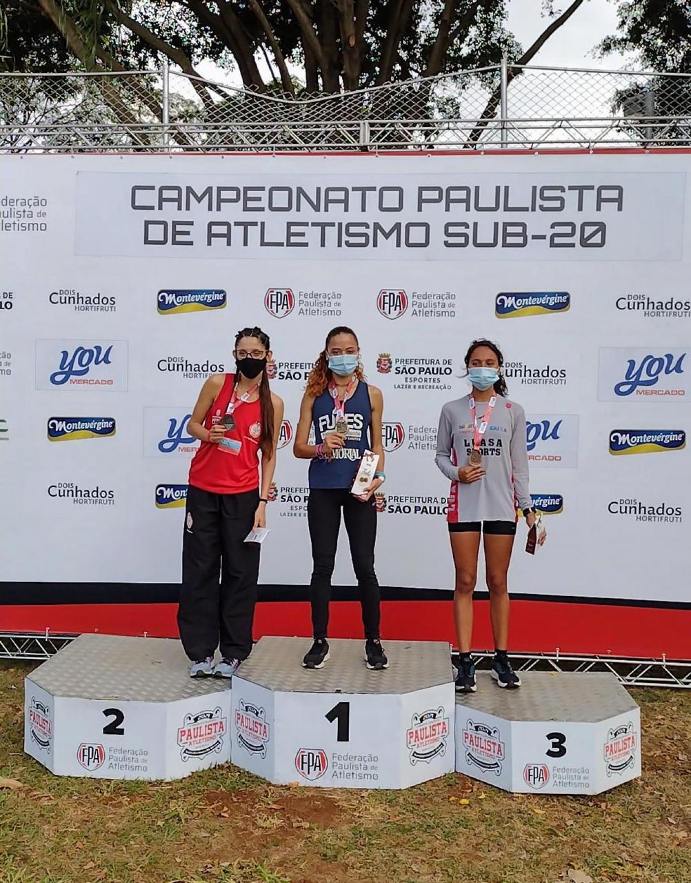 Pódio com três jovens. Ao centro, no primeiro lugar, está caroline dias. #paratodosverem