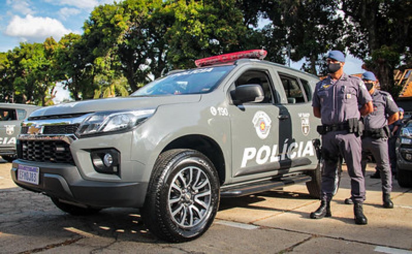 Viatura estacionada com dois policiais fardados ao lado. #pracegover