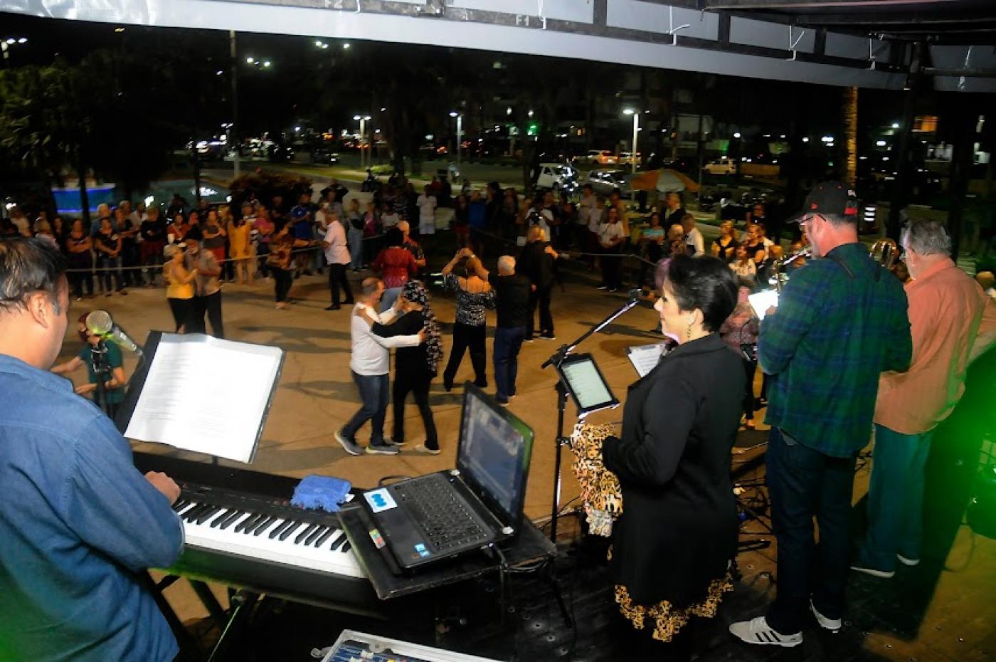 banda musical sobre palco em primeiro plano e casais dançando na pista. #paratodosverem