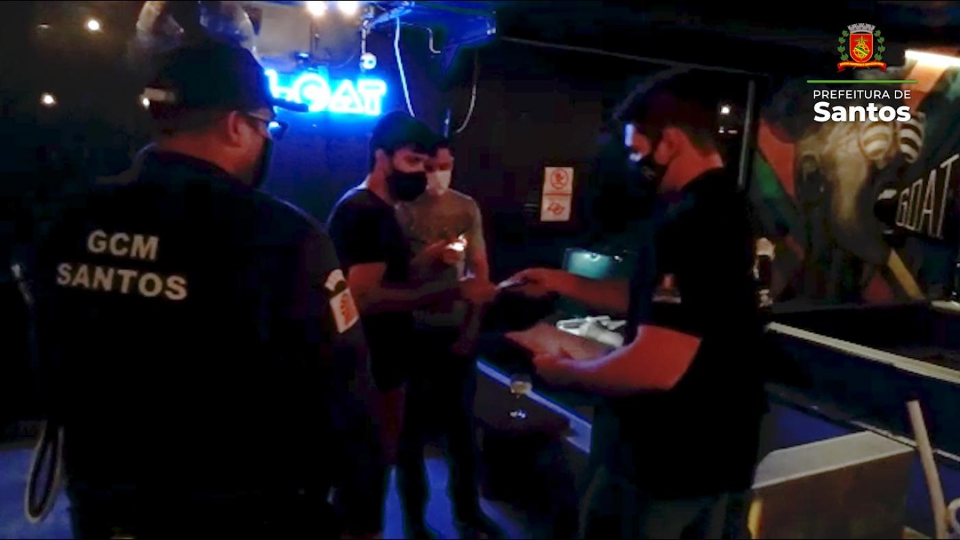 dois guardas municipais entregam documento para dois homens dentro de bar. #paratodosverem