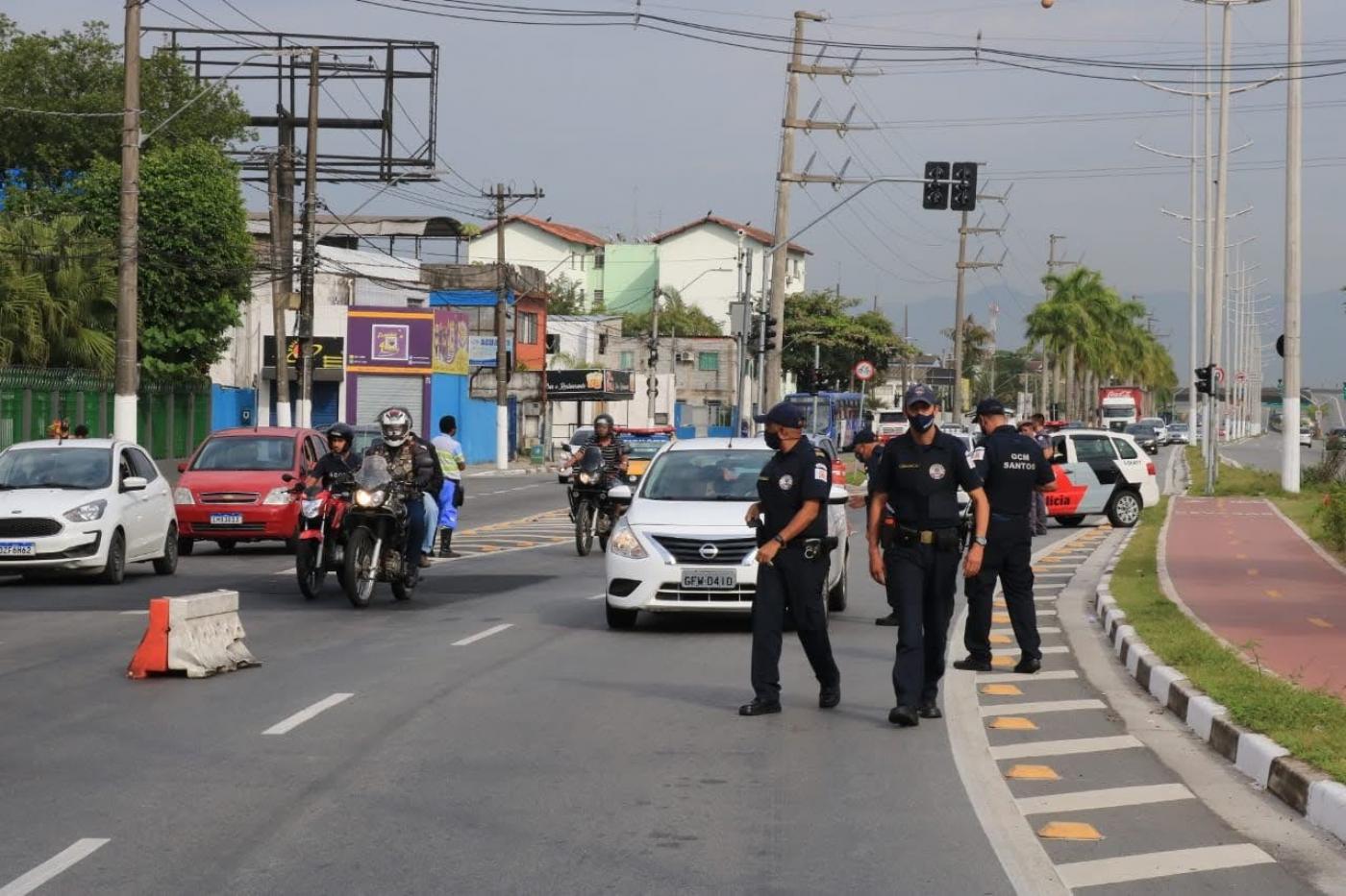 guardas municipais caminham em pista demarcarda por barreiras no centro. Carros e motos também trafegam. #paratodosverem