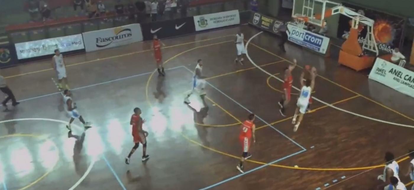 Jogador vestido de uniforme branco arremessa bola marcado por jogador de vermelho e outros atletas em volta. na quadra de basquete. #pratodosverem