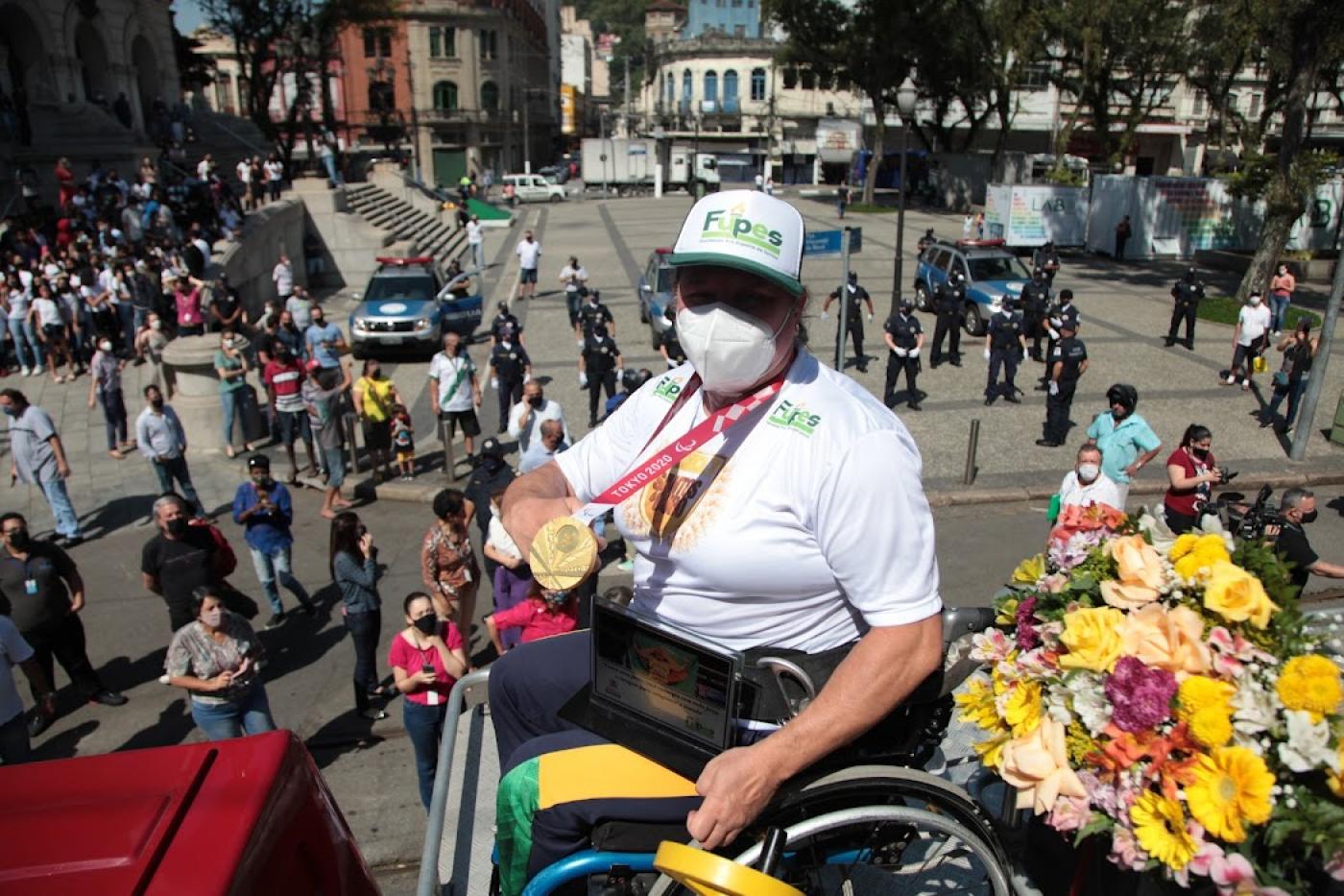 Beth em cima do carro do Corpo de Bombeiros exibe medalha com várias pessoas ao fundo. #paratodosverem