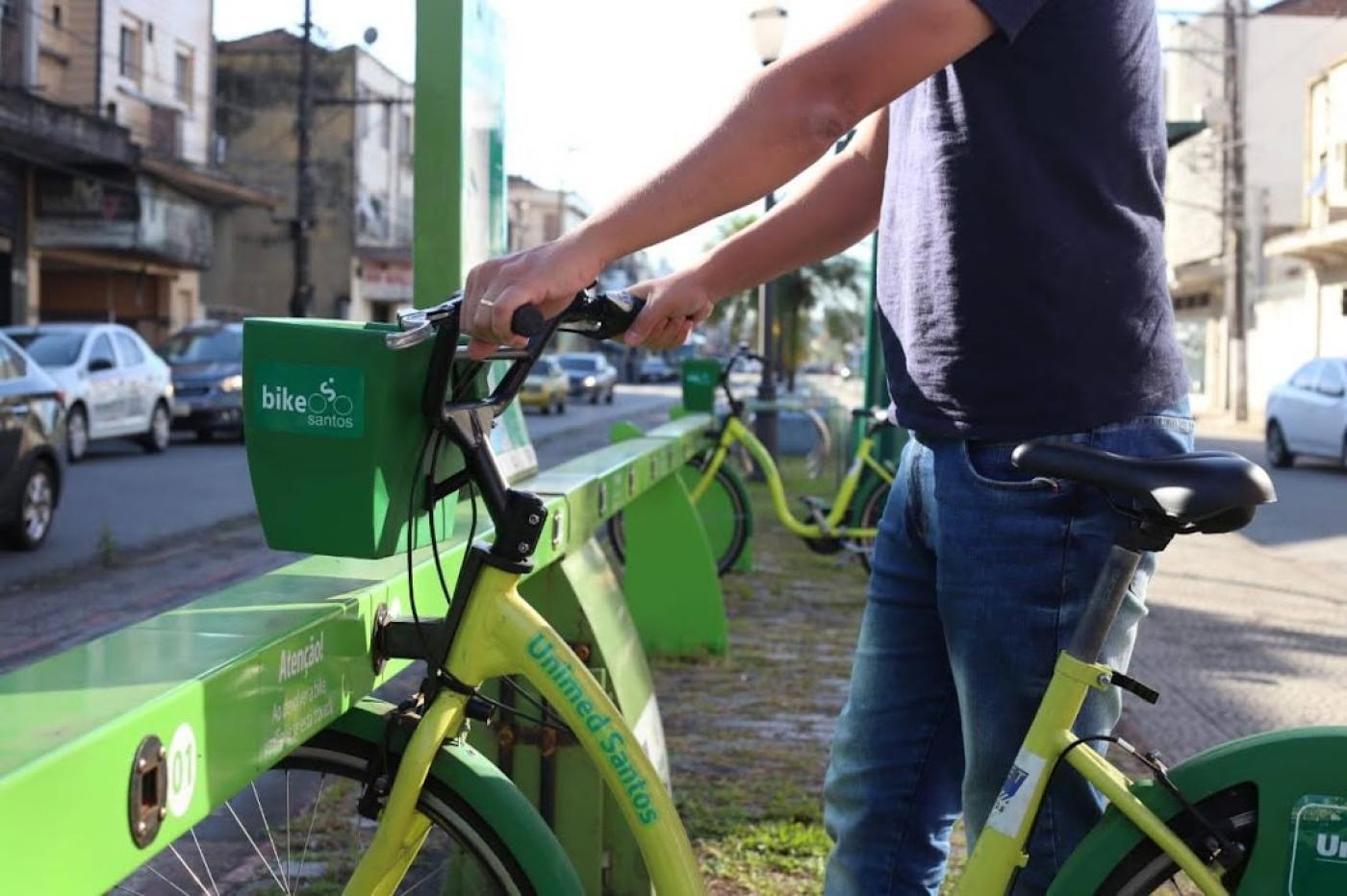 Homem segura bicicleta em uma estação do Bike Santos. #paratodosverem