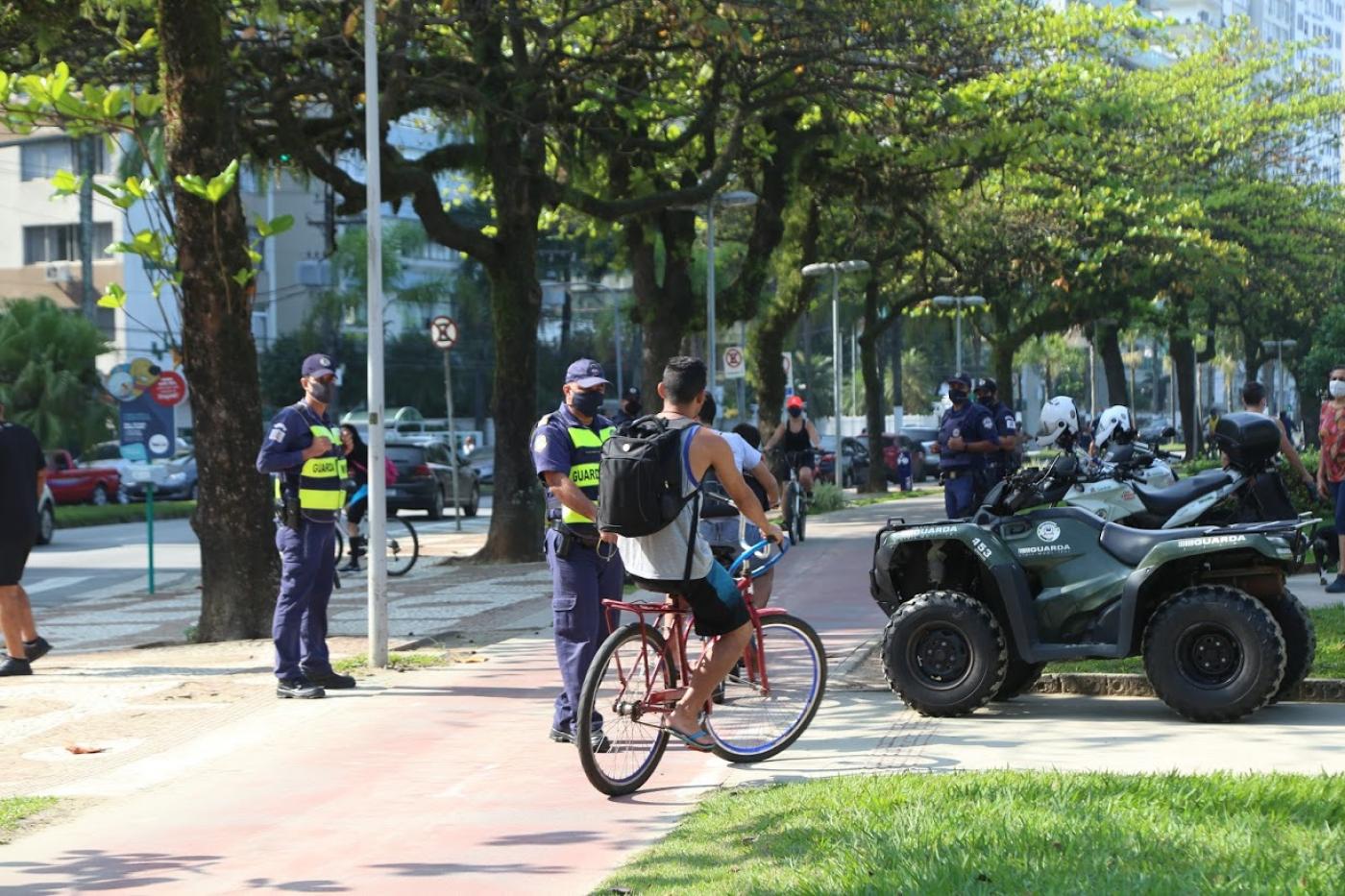 Dois guardas estão junto a ciclovia. Um ciclista está passando. 