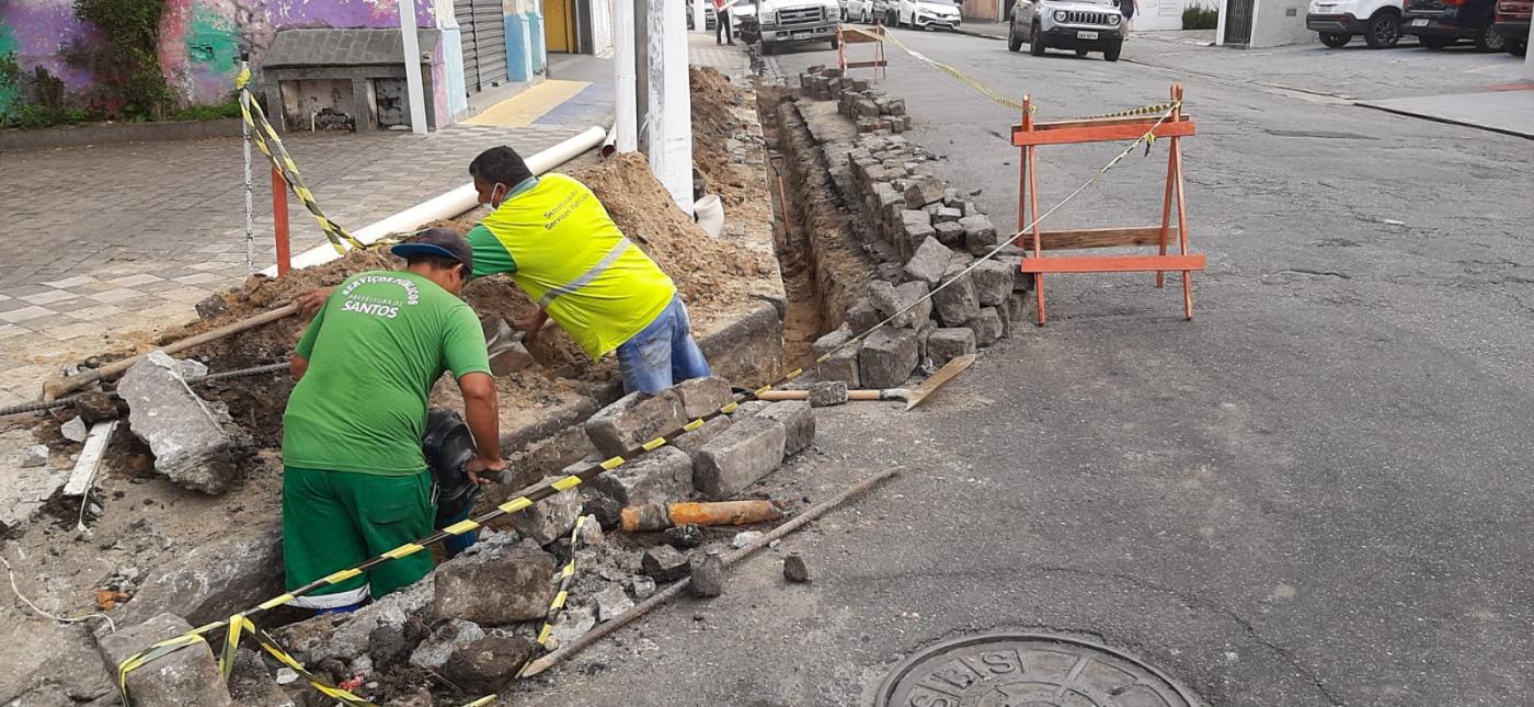 Homens trabalham na construção de bocas-de-lobo na via. #paratodosverem