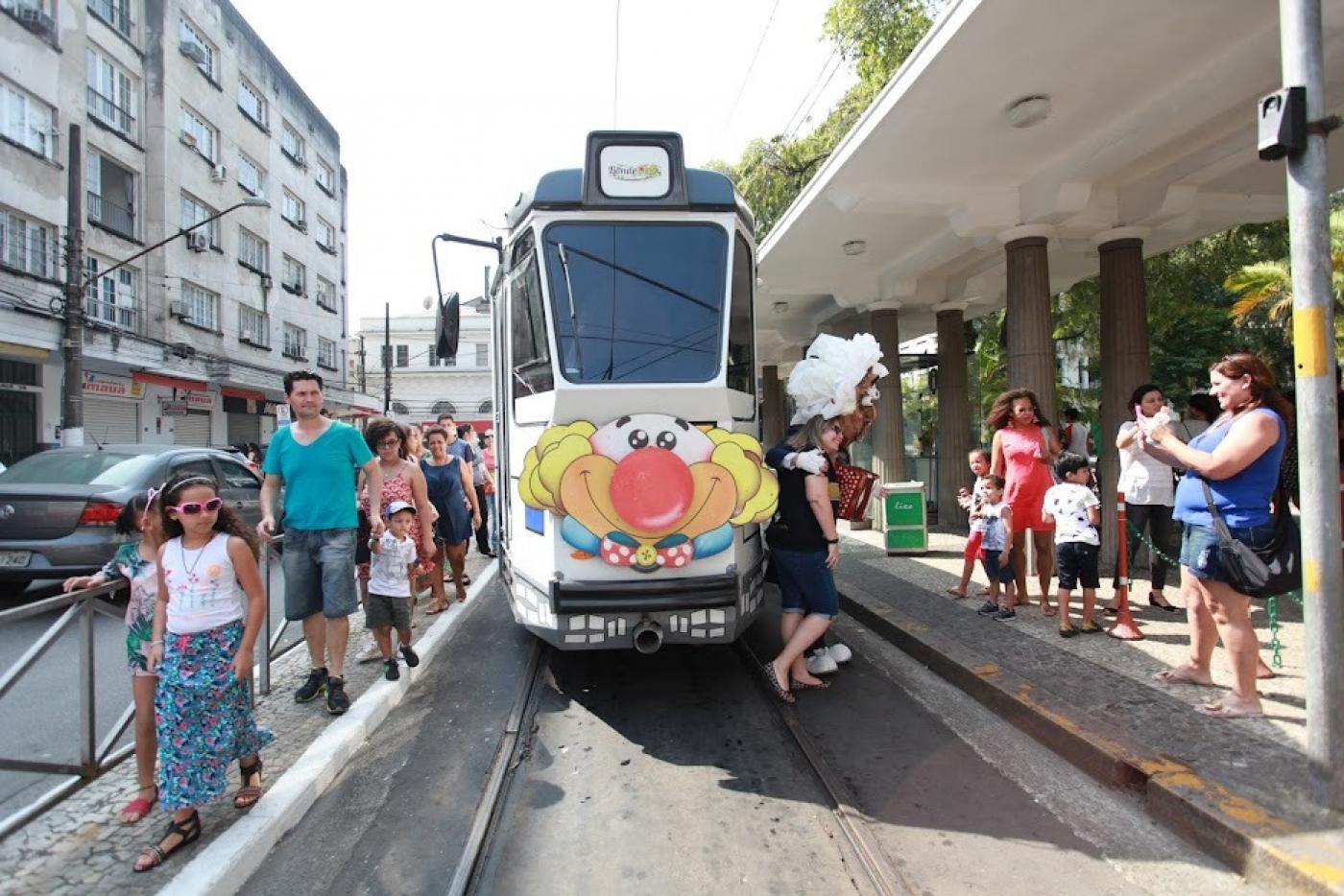 Bonde colorido no trilho e vários pais e crianças ao lado #paratodosverem