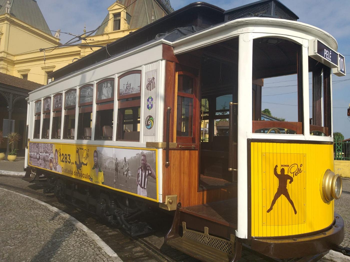 carro de bonde parada sobre os trihos. A frente é decorada com a imagem de pelé dando soco no ar. Laterais também têm imagens do rei do futebol. #paratodosverem