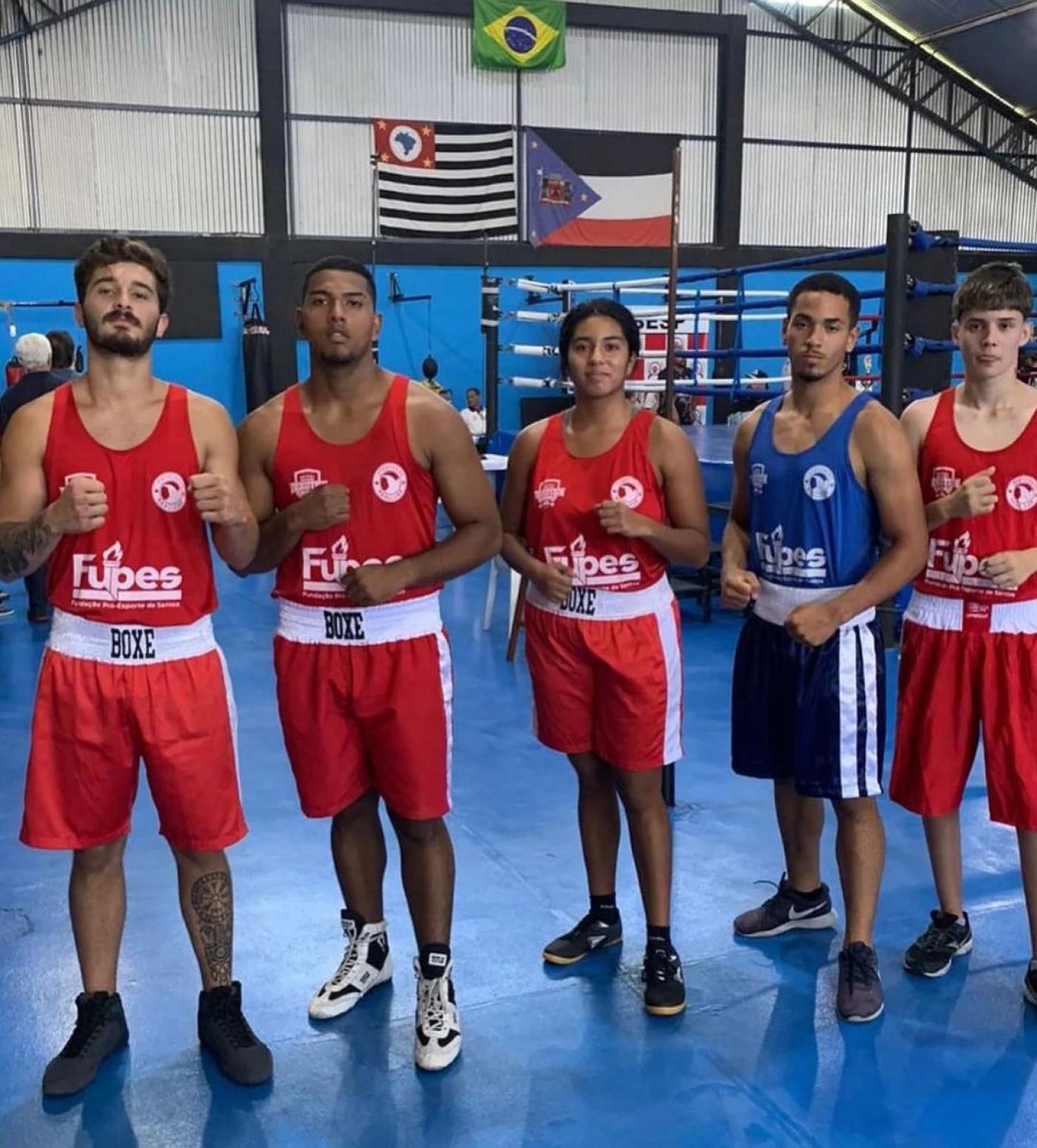 cinco boxeadores, sendo quatro homens e uma mulher ao centro, posam para a foto com as mãos em gesto de luta. #paratodosverem