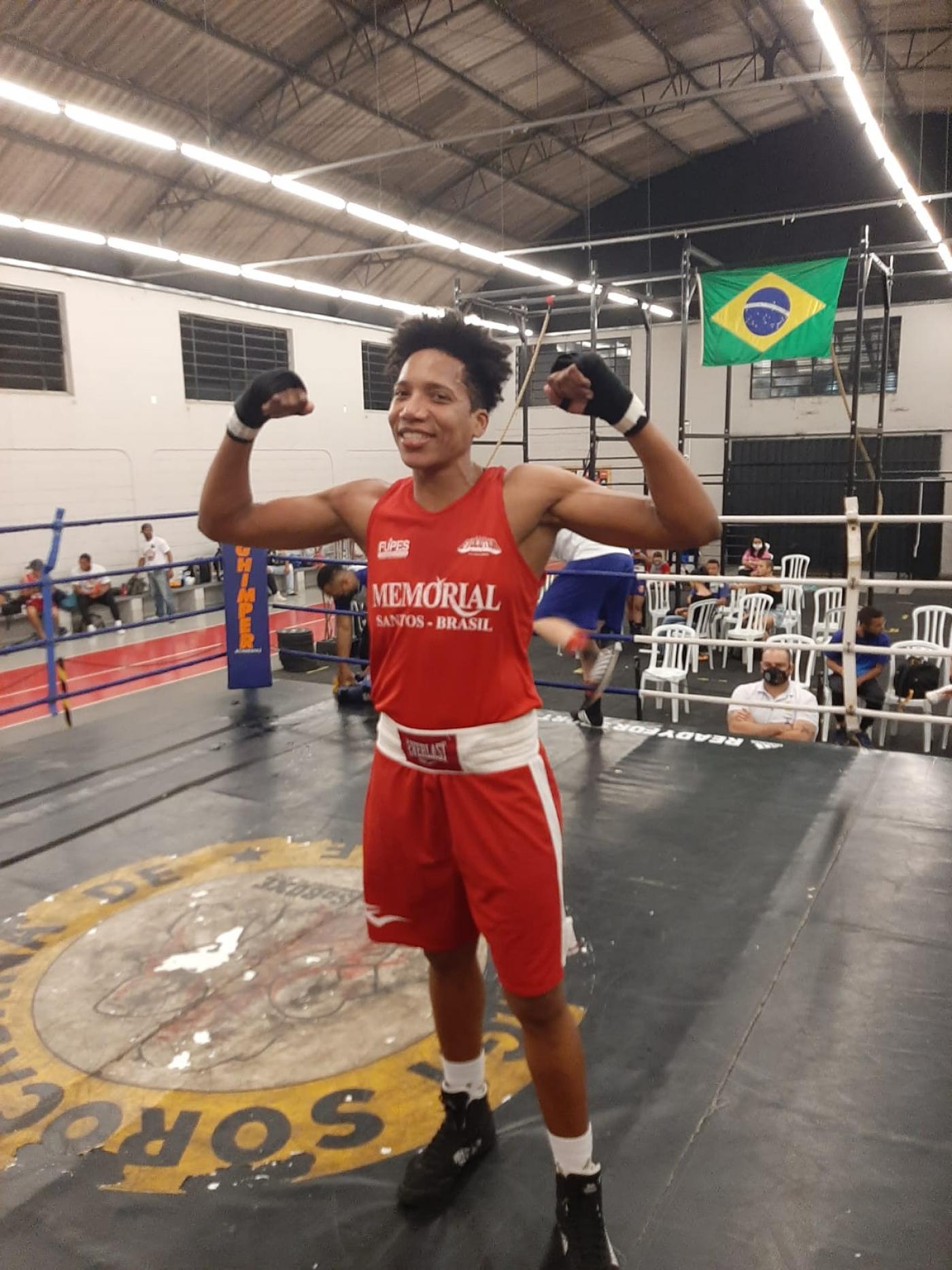 a boxeadora  no ringue faz gesto de vitória com os dois braços erguidos lateralmente. #paratodosverem