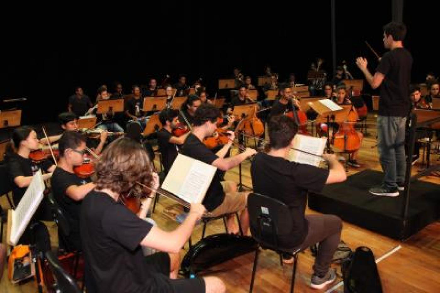 músicos de uma orquestra se apresentam em palco. #paratodosverem 