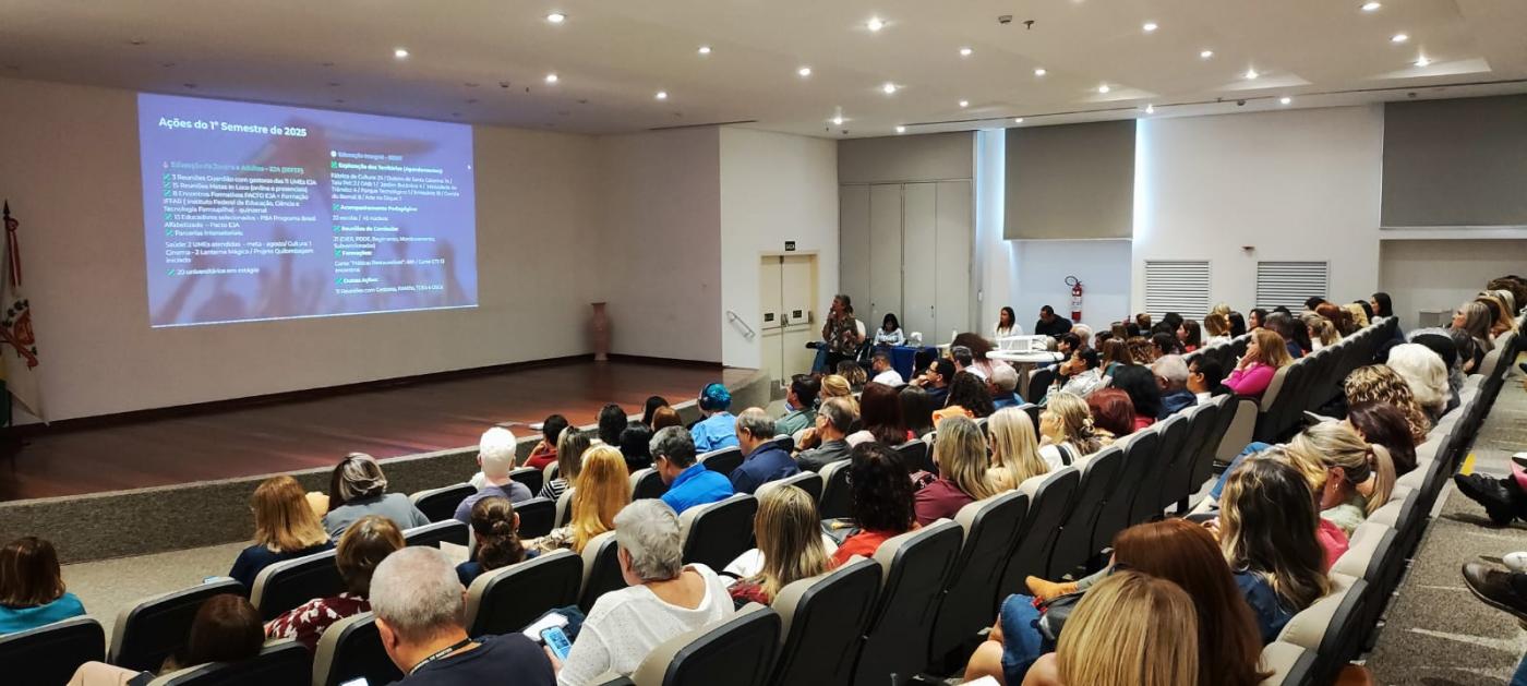servidores sentados em auditório assistindo palestra. #paratodosverem