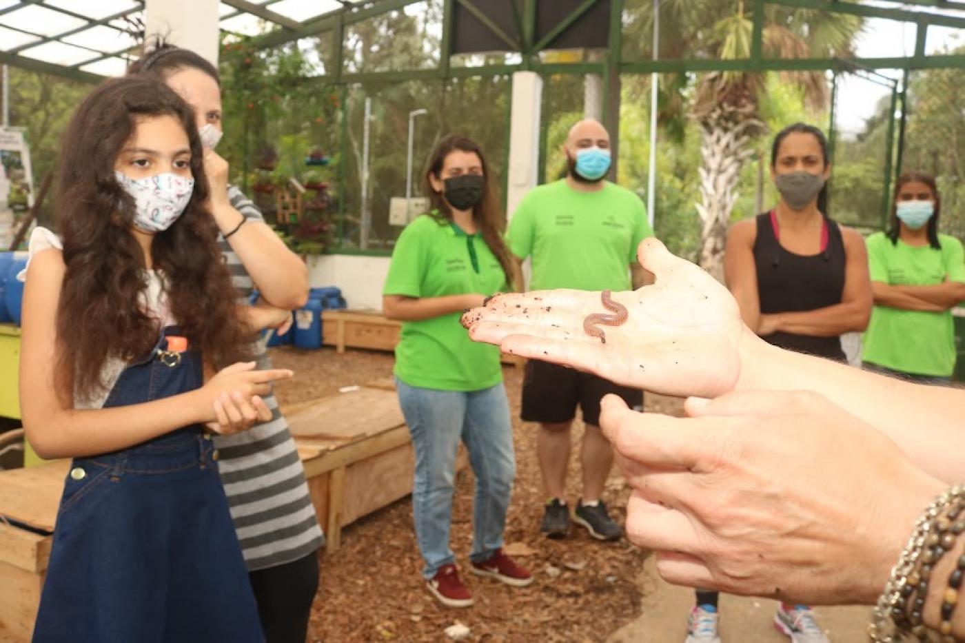 homem mostra minhoca que faz processo de compostagem a visitantes. 