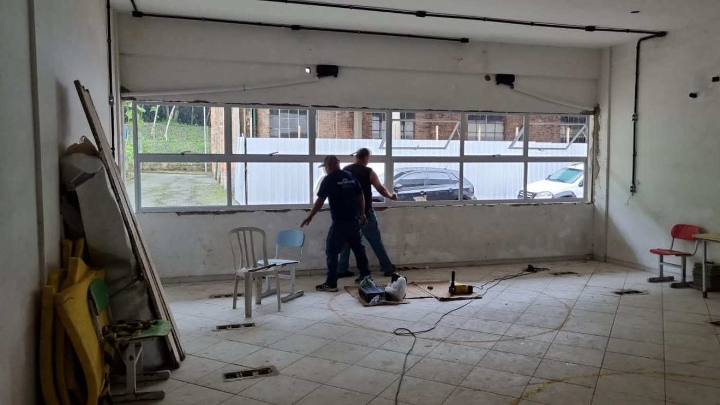 dois homens trabalhando próximo a uma janela em uma sala. #paratodosverem 