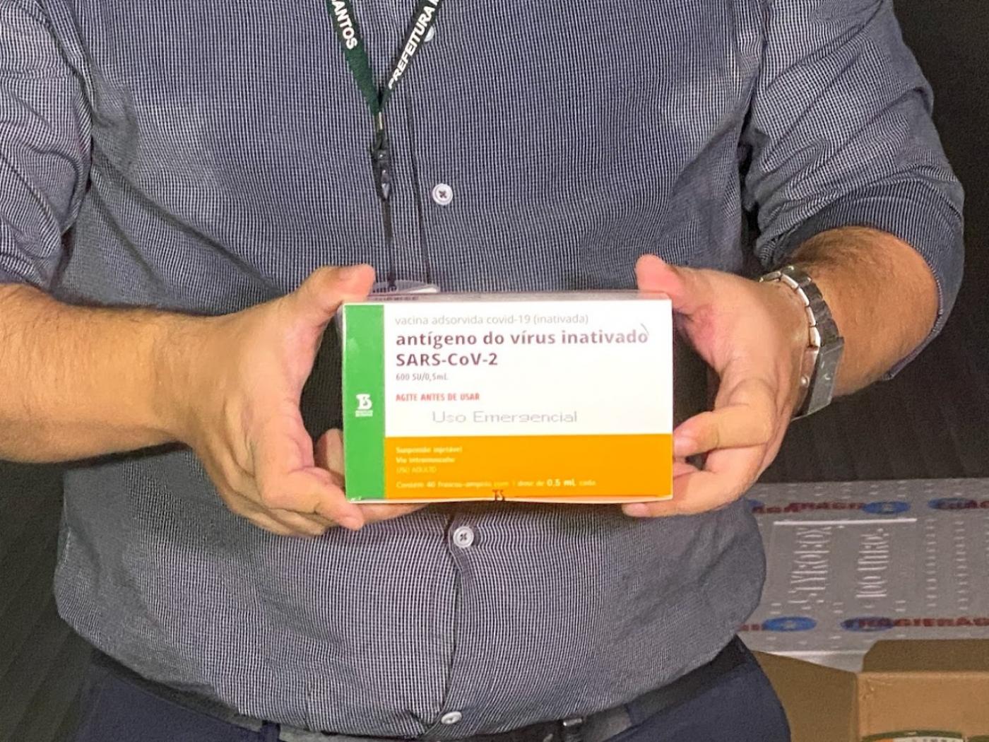imagem em close com mãos de homem segurando caixa com doses de coronavac. #paratodosverem