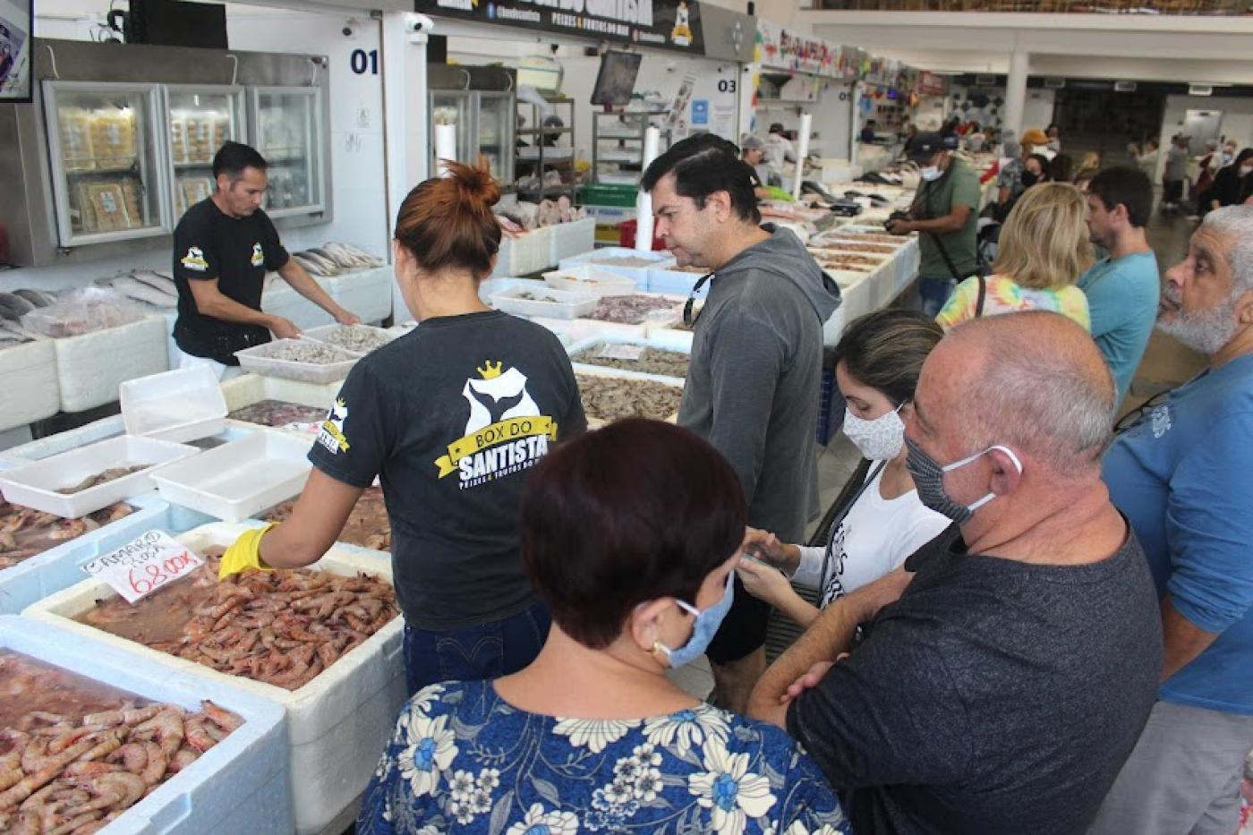 várias pessoas em frente a box de venda de peixes. Caixas de isopor contêm muitos camarões e de espécies variadas. #paratodosverem