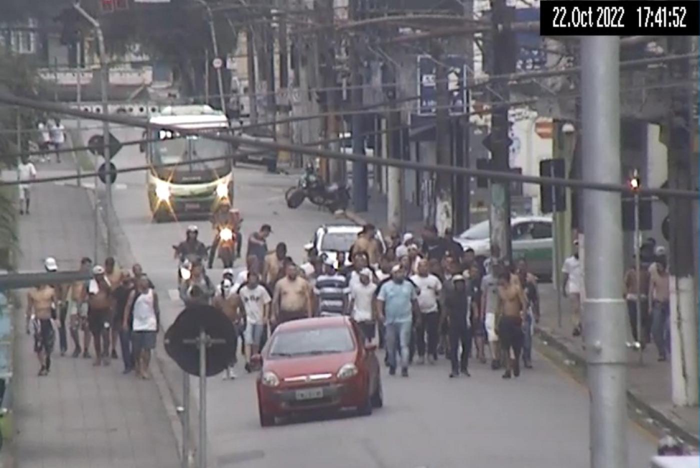 vários homens caminhando por rua atrás de um carro vermelho. #paratodosverem