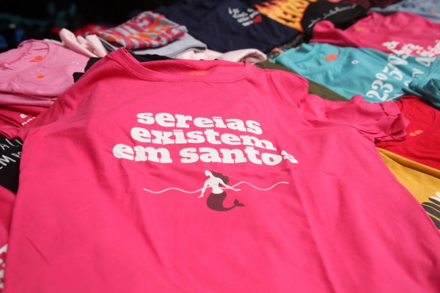 camiseta onde se lê Sereias existem em Santos. Arte é de uma sereia no mar. #paratodosverem