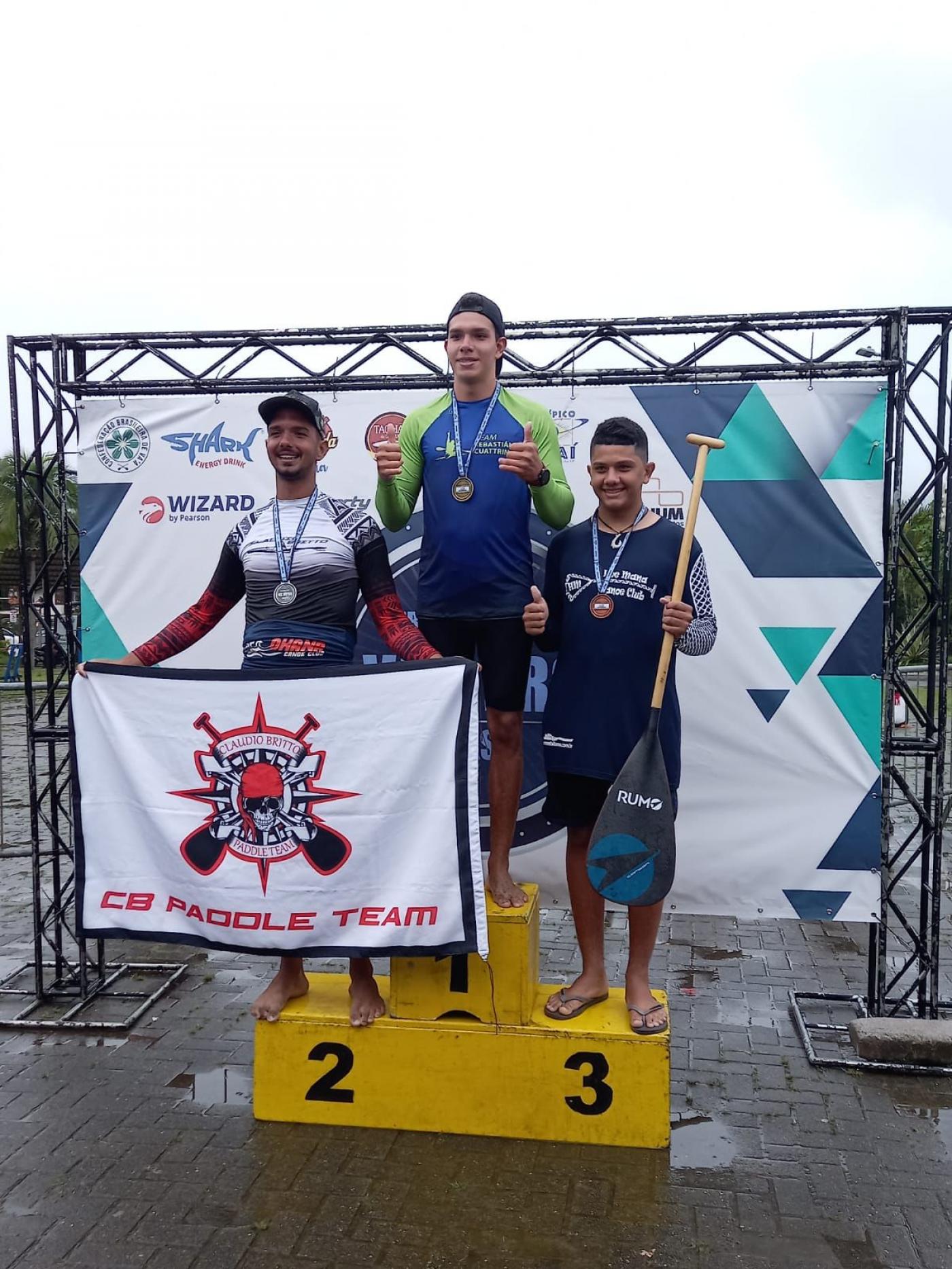 Atletas no pódio com medalha #paratodosverem