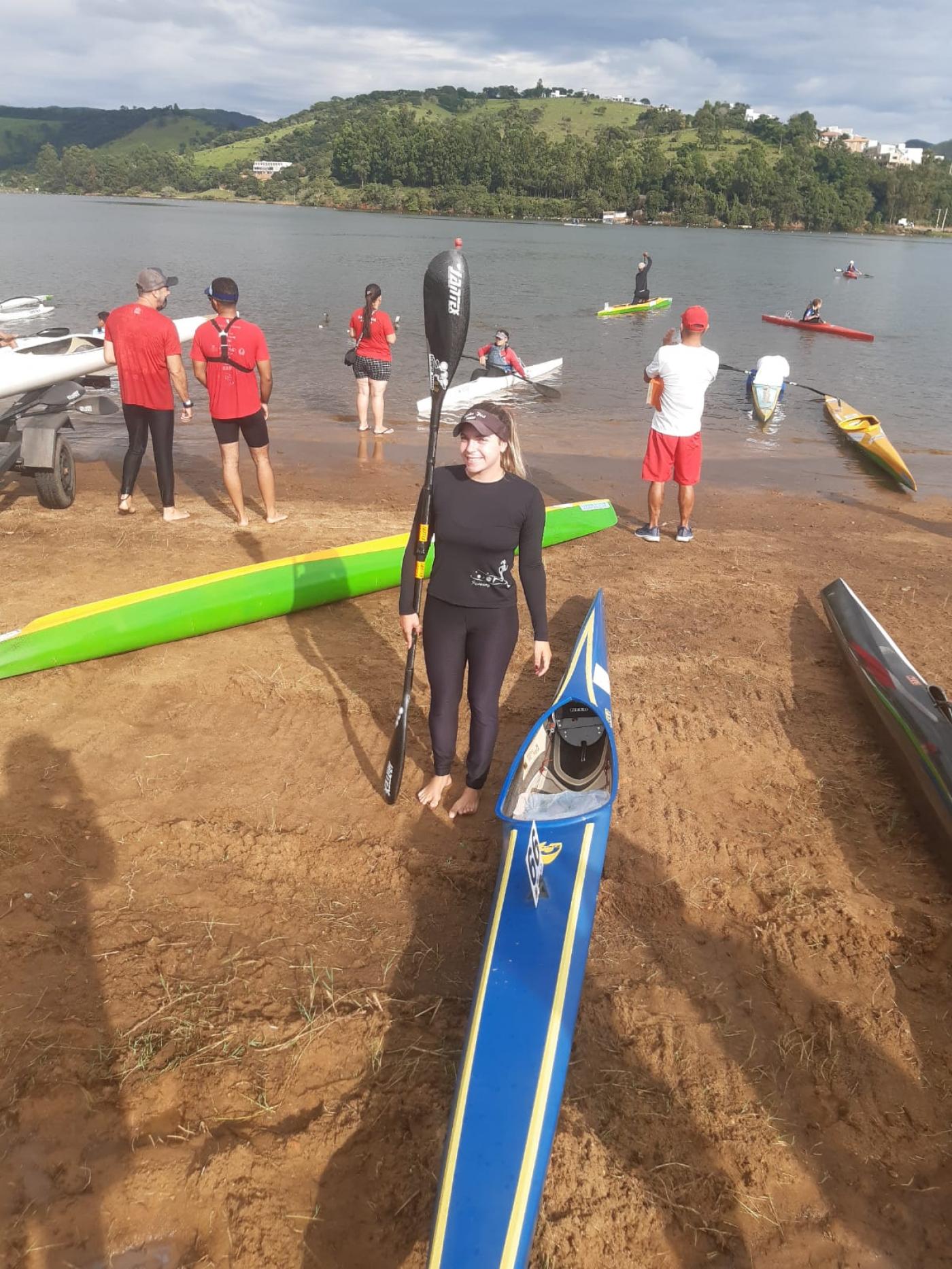 bruna posa para foto em beira de rio, ao lado da canoa. #paratodosverem