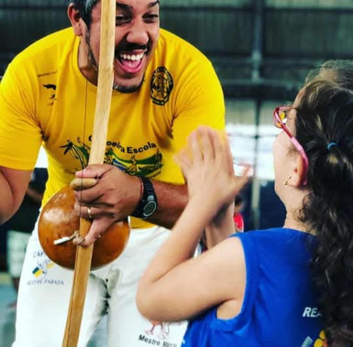 mestre toca berimbau diante de criança. #paratodosverem